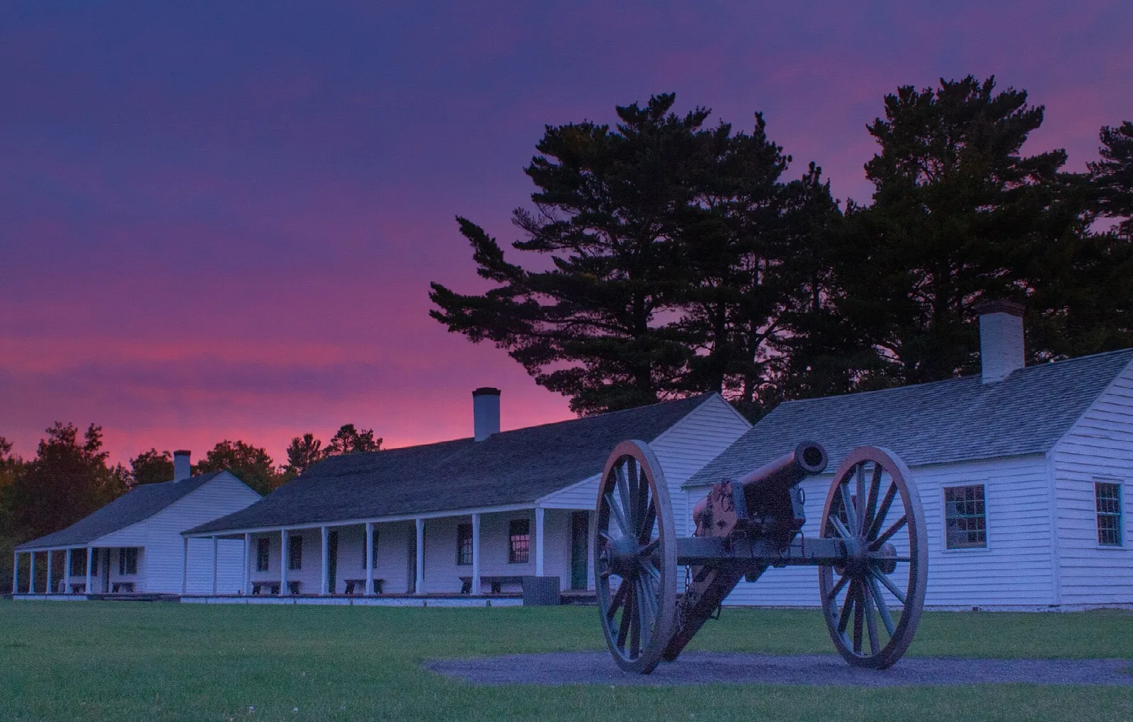 White fort barracks with a cannon in front under a pink and purple sunrise sky