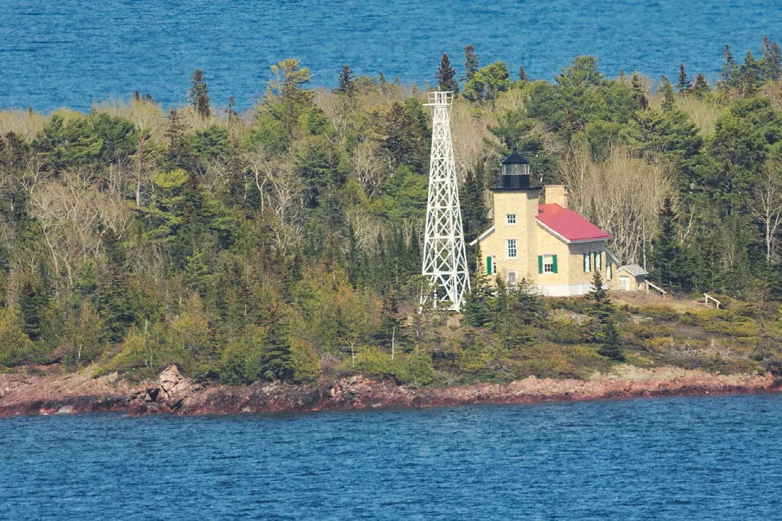 Lighthouse and steel tower on a wooded shoreline beside the lake