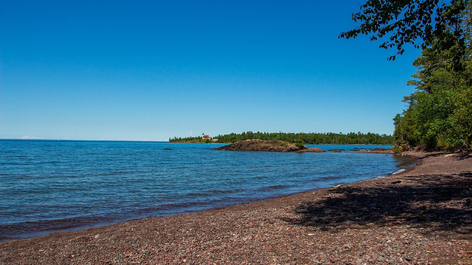 Pebble beach and blue lake water with a small wooded island in the distance