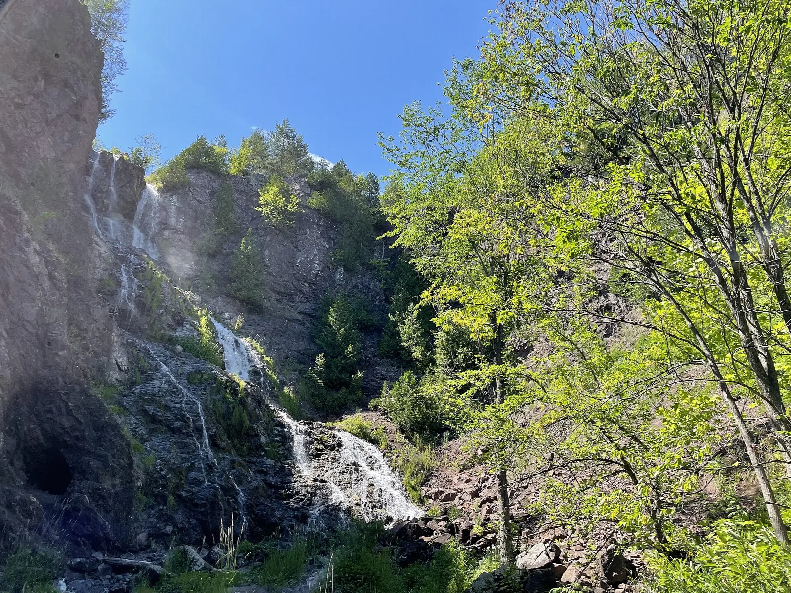Waterfall tumbling down a rock cliff beside green leafy trees