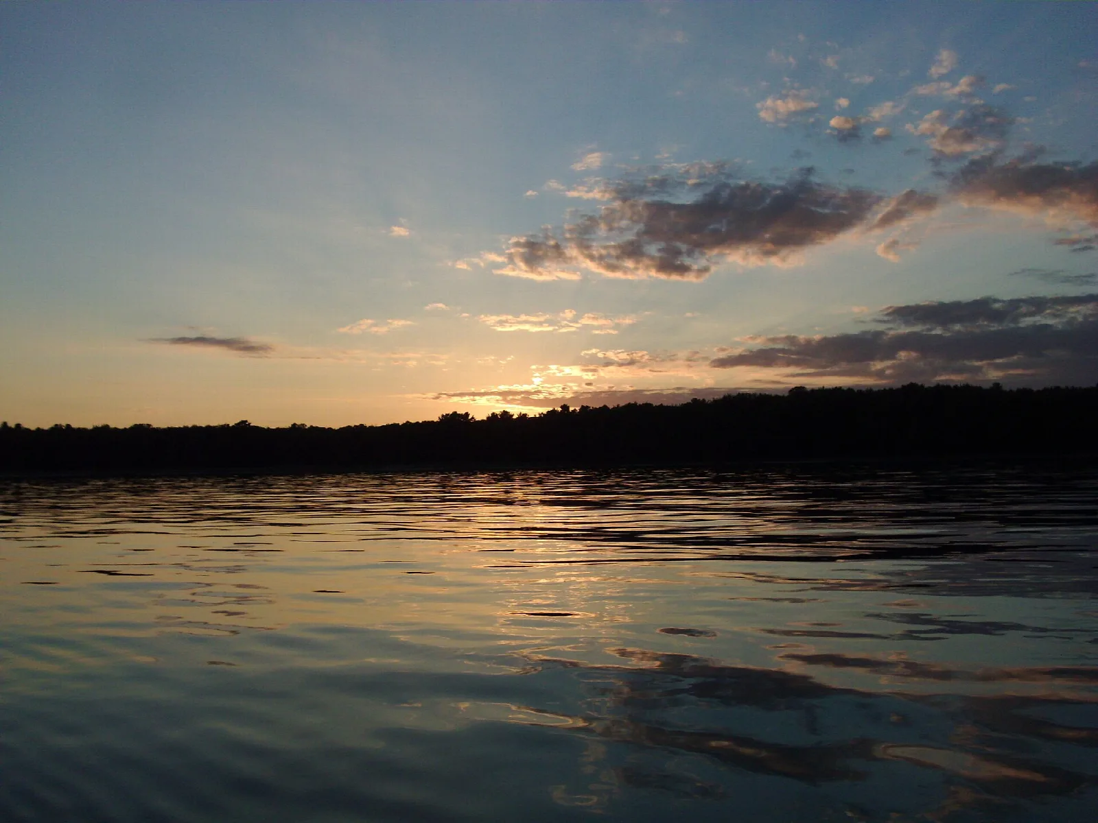 Sunset sky over dark treeline and calm water