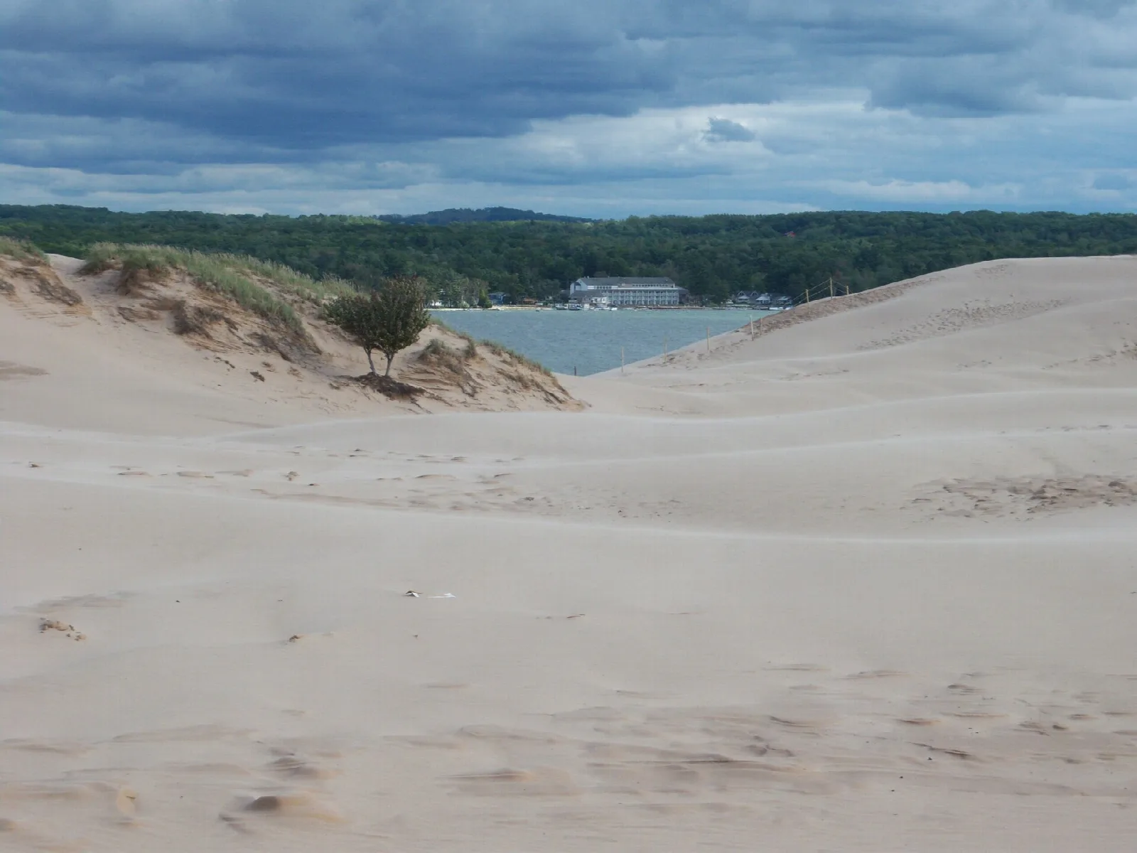 Open dunes with a lake and treeline in the distance under dark clouds