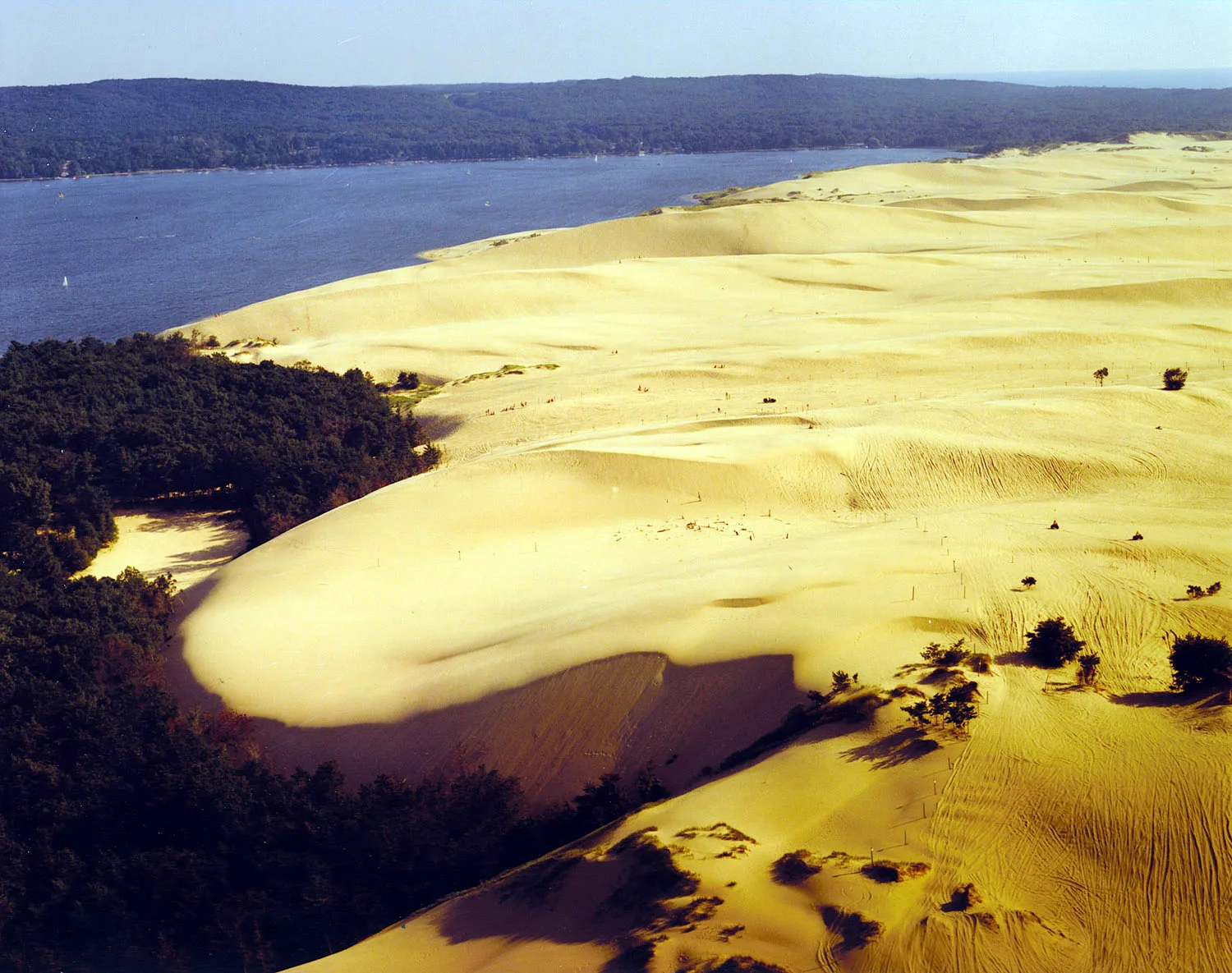 Aerial view of a large pale sand dune running down to a lake