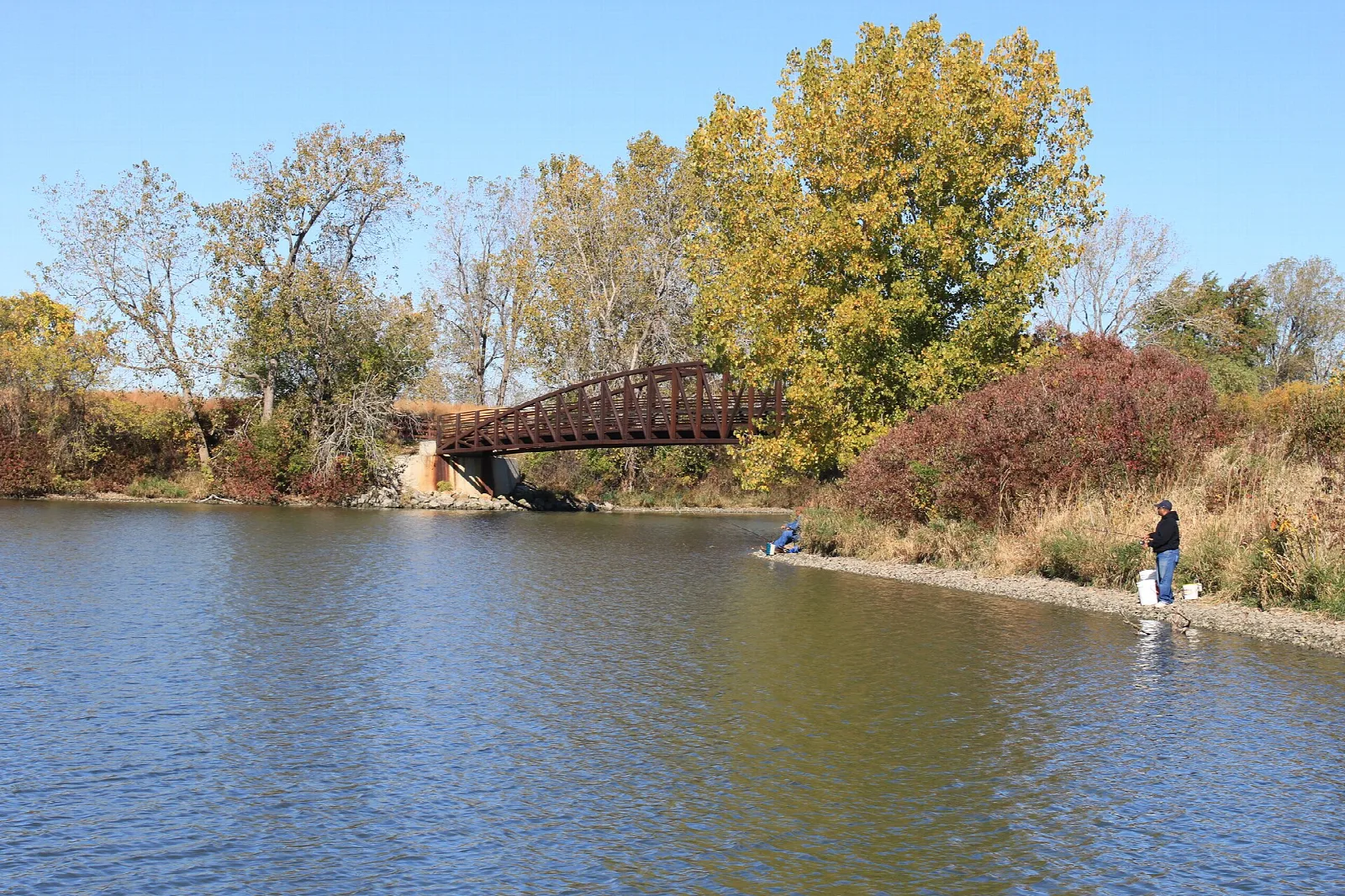 Red footbridge over a lagoon with autumn trees and an angler