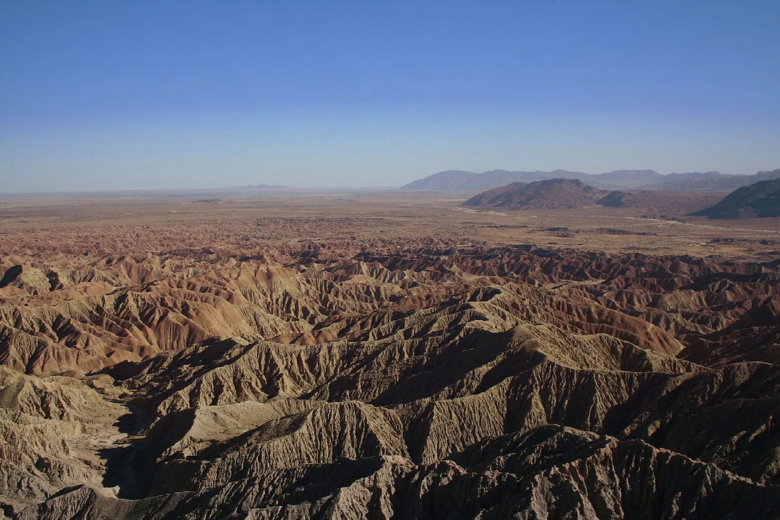 Wide view over eroded badlands toward distant desert mountains