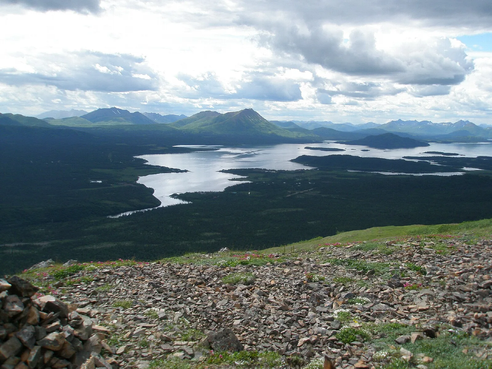 Wide lake and river valley seen from a rocky hillside under a cloudy sky