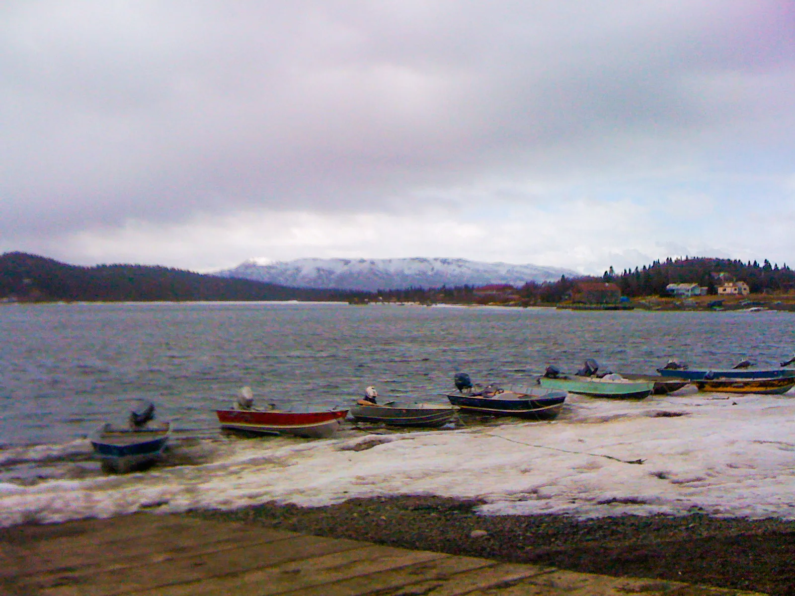 Small boats pulled up on a gravel beach by a lake with distant snowy hills