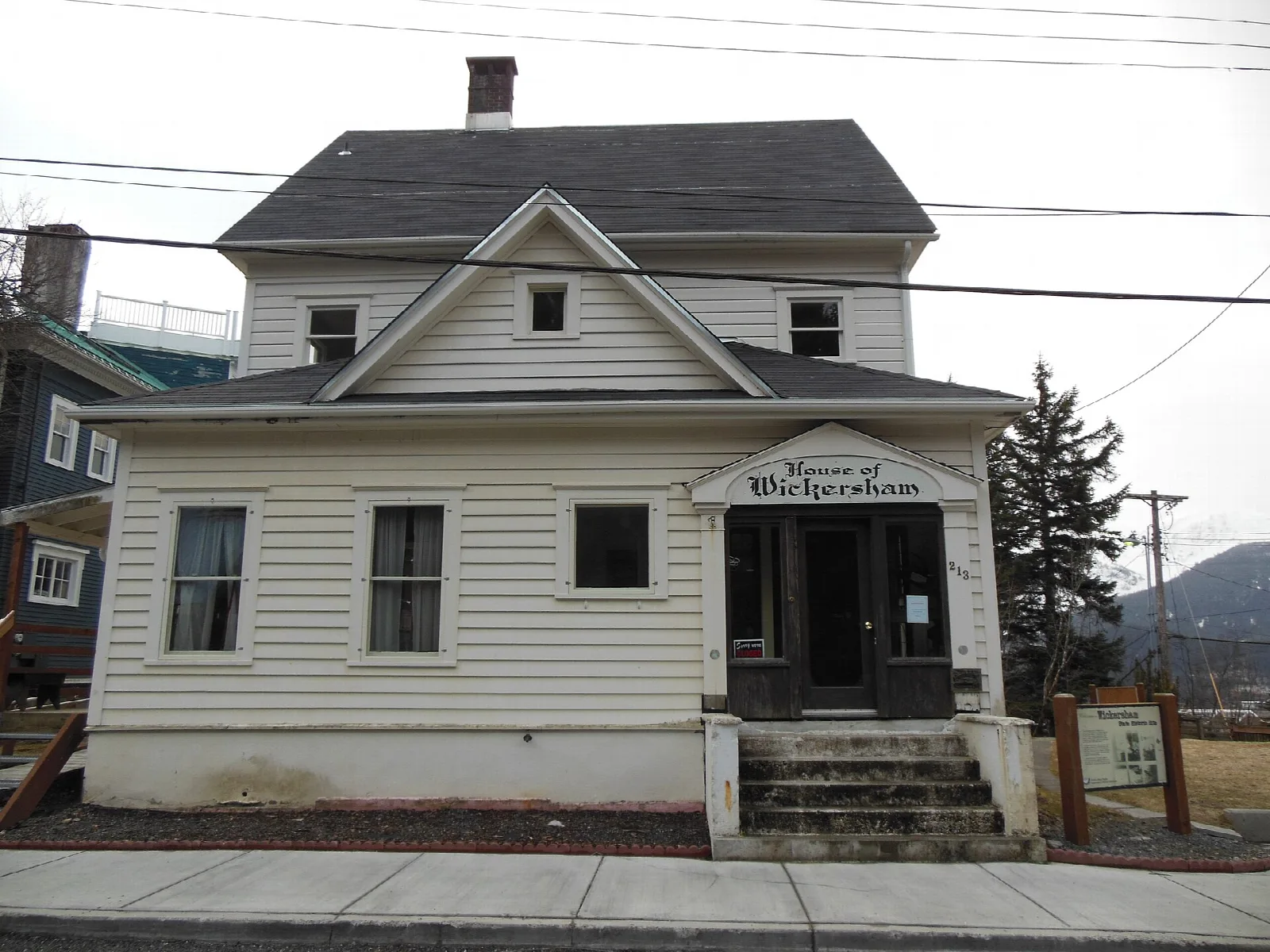 White two-story wooden house with a sign reading House of Wickersham