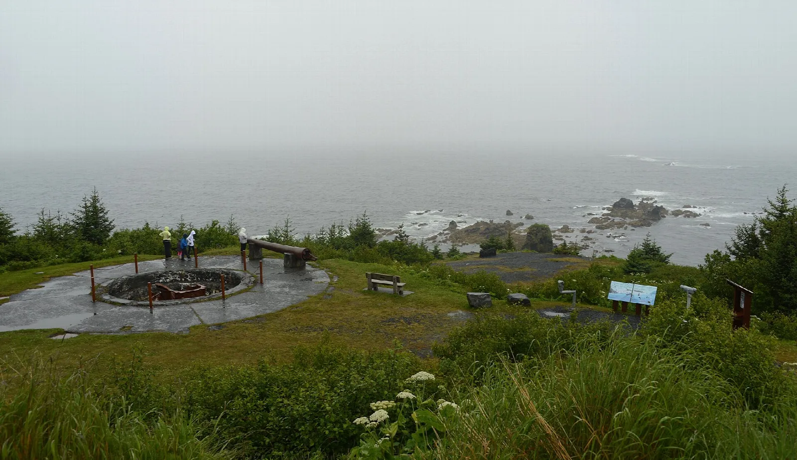 Grassy headland with a circular concrete overlook and viewing benches above a misty sea