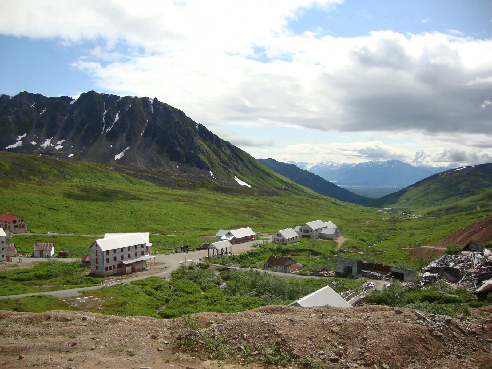 White mine buildings in a green valley below dark rocky peaks