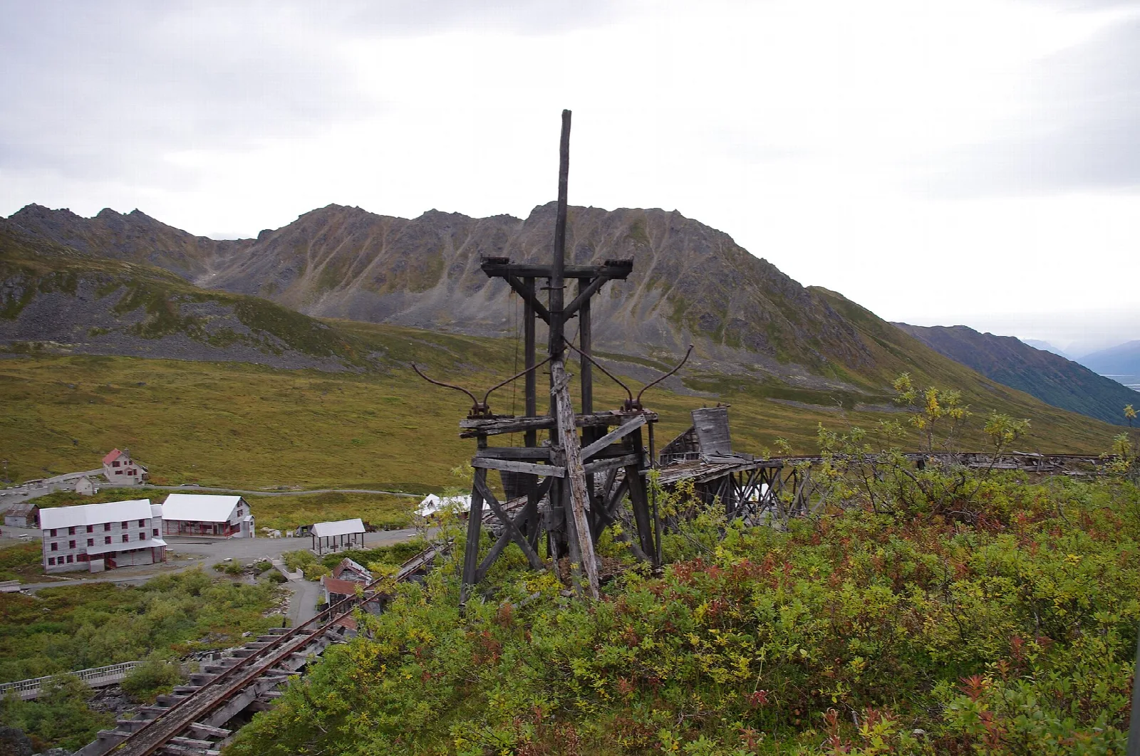 Wooden tower and rail track in front of old mine buildings and mountains