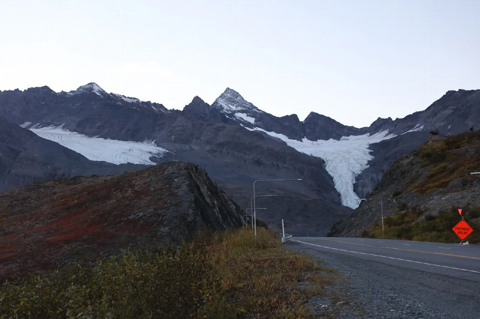 Snowy glacier tongue between dark mountains beside a highway