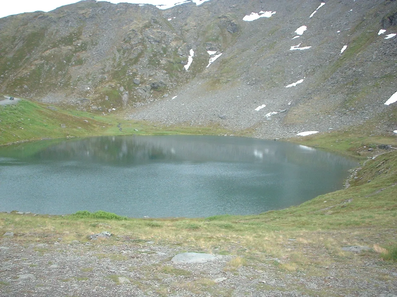 Small mountain lake with green slopes and patches of snow above it