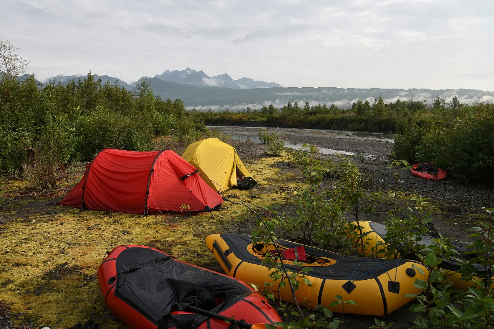 Red and yellow tents and inflatable rafts on a gravel bar by a river