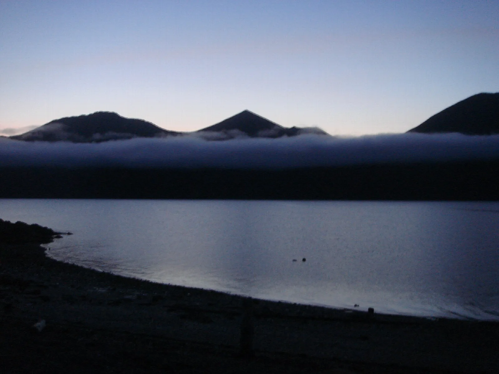 Dark mountain ridges above a low fog bank over still water at dusk