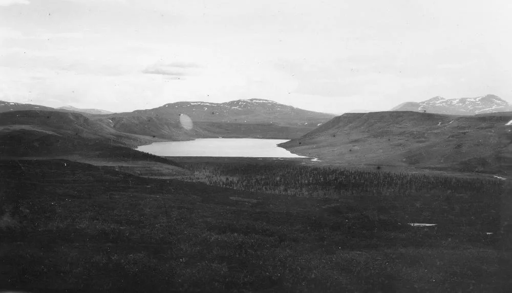 Black-and-white survey photo of a lake in open tundra with low hills and distant peaks