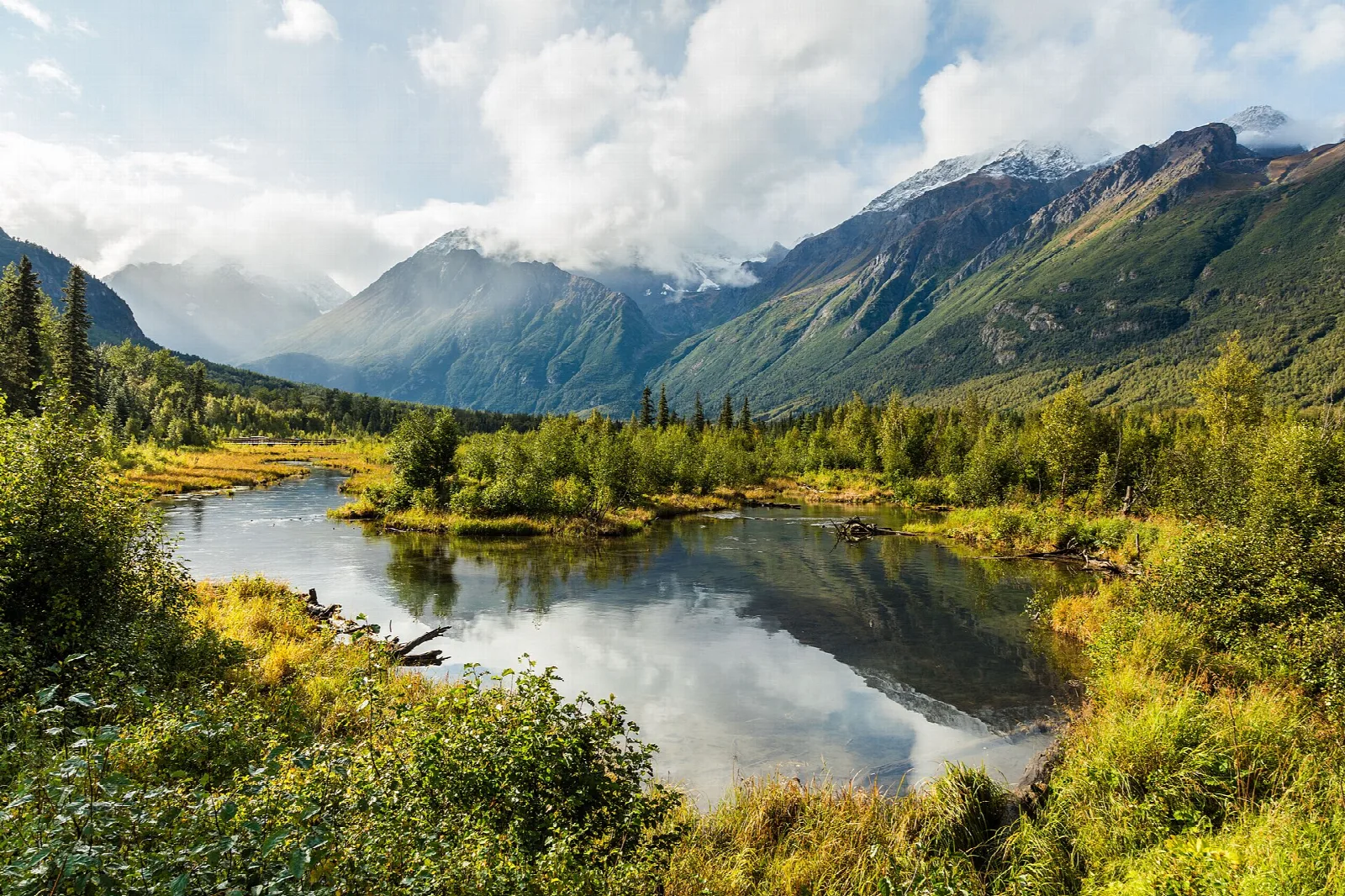 A calm lake in a green valley with mountains and clouds beyond