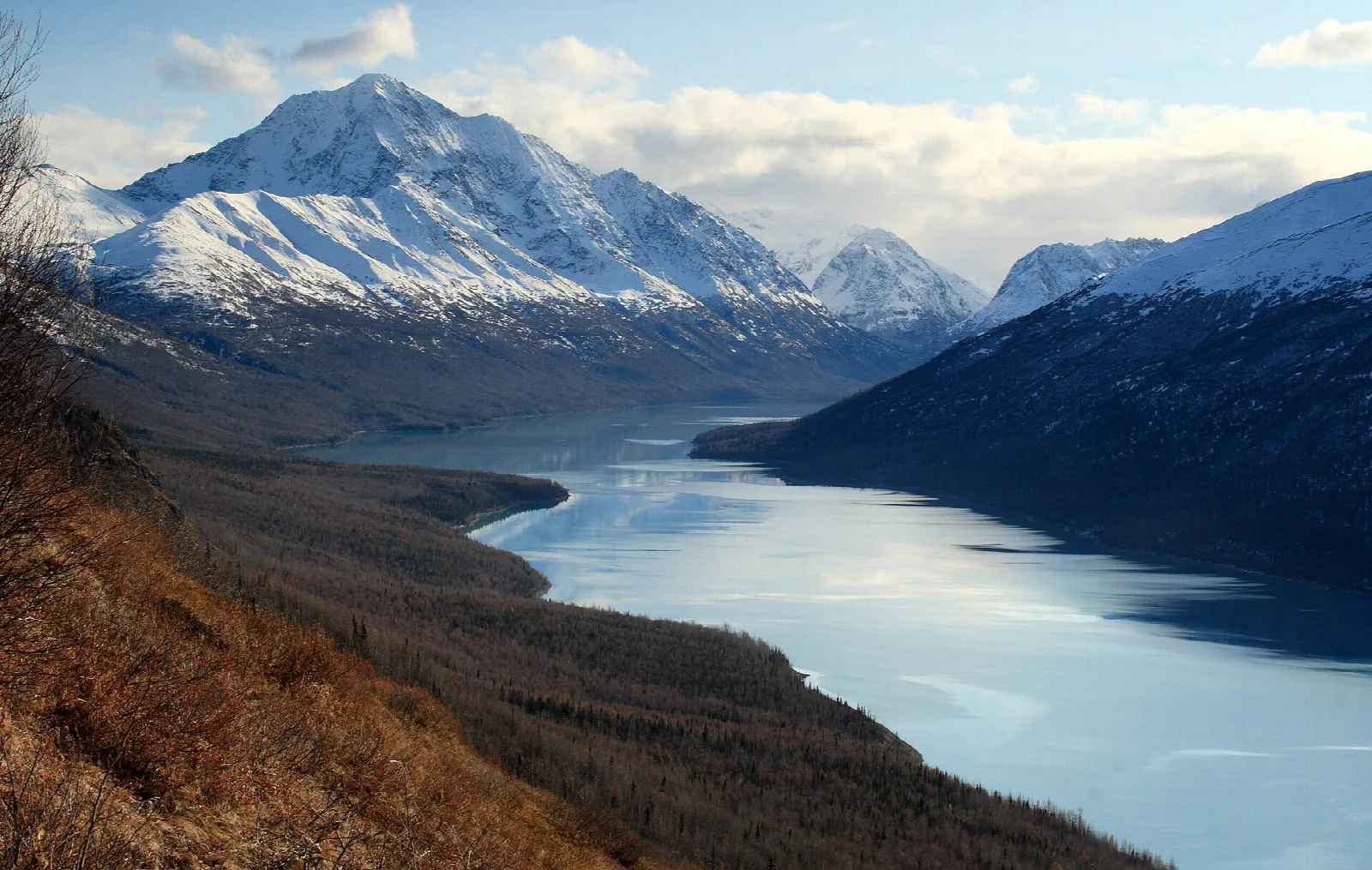 A long blue lake between steep mountains with a snowy peak at the end