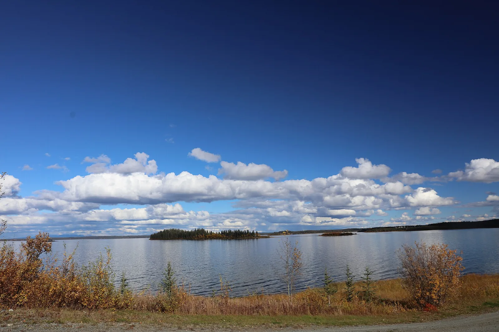 A wide lake with small wooded islands under a deep blue sky