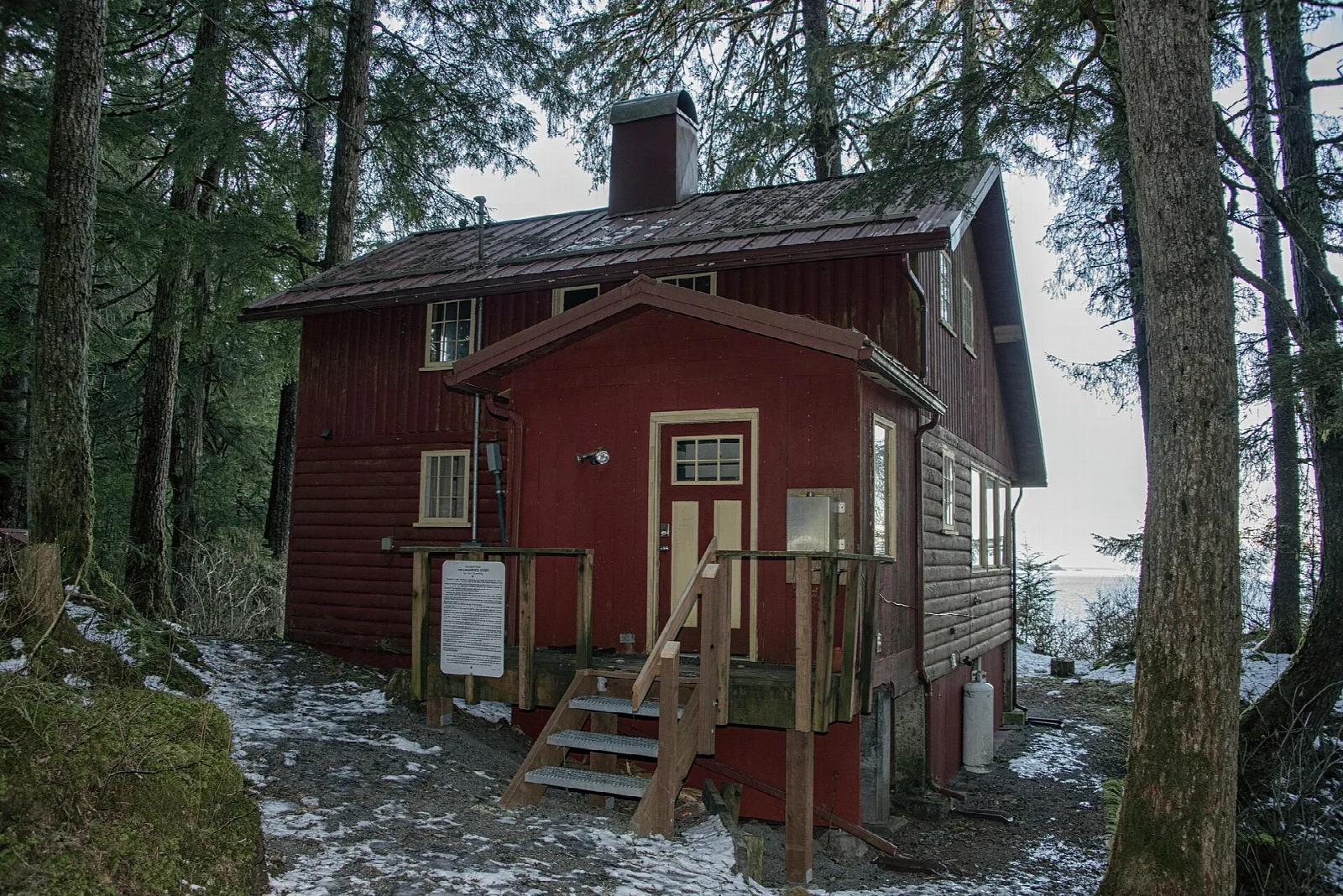 A dark red cabin entrance with steps in a snowy spruce forest