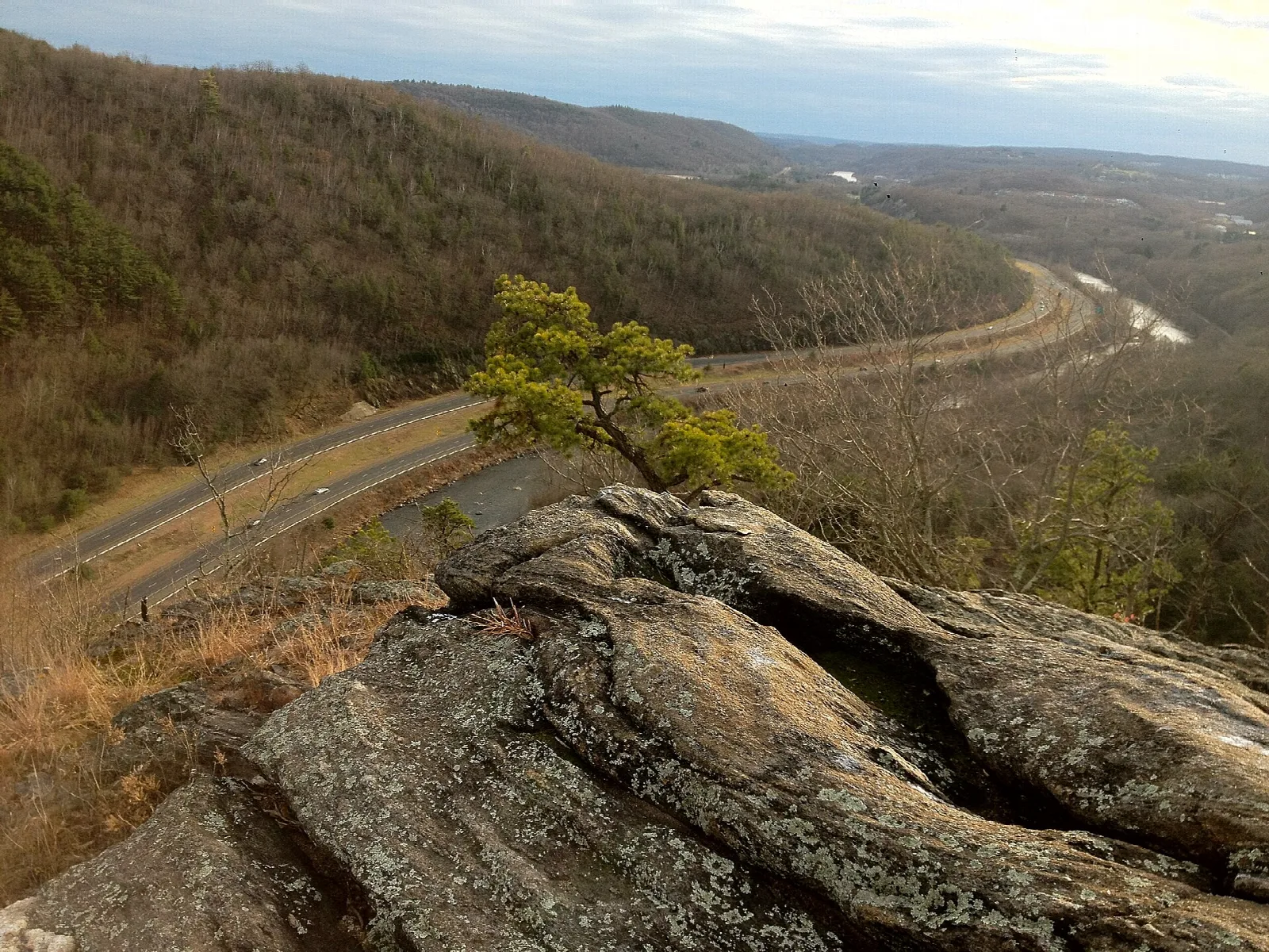A river valley with a highway and wooded hills below a rocky lookout