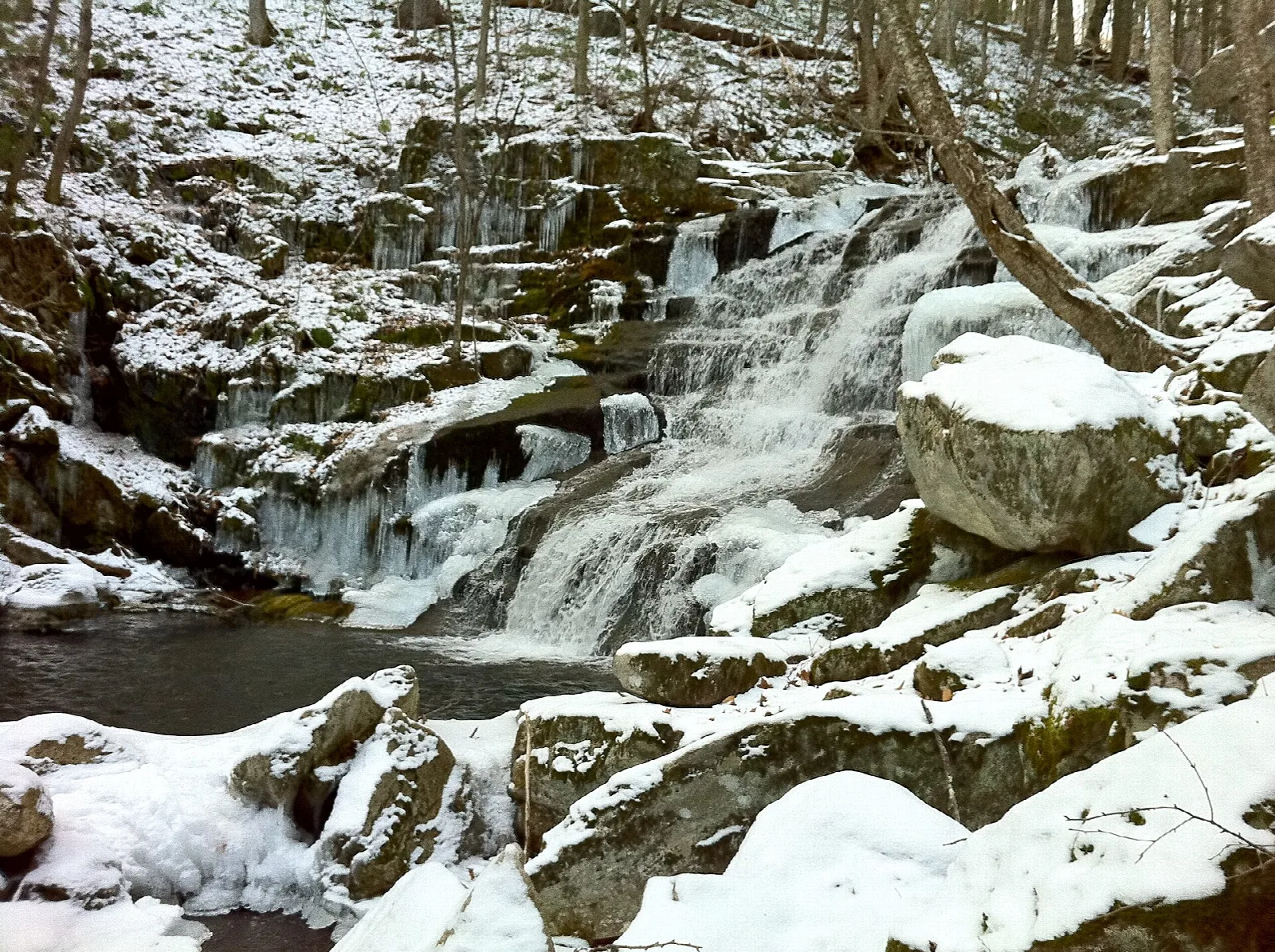 A snow-covered waterfall tumbling over rocks into a pool