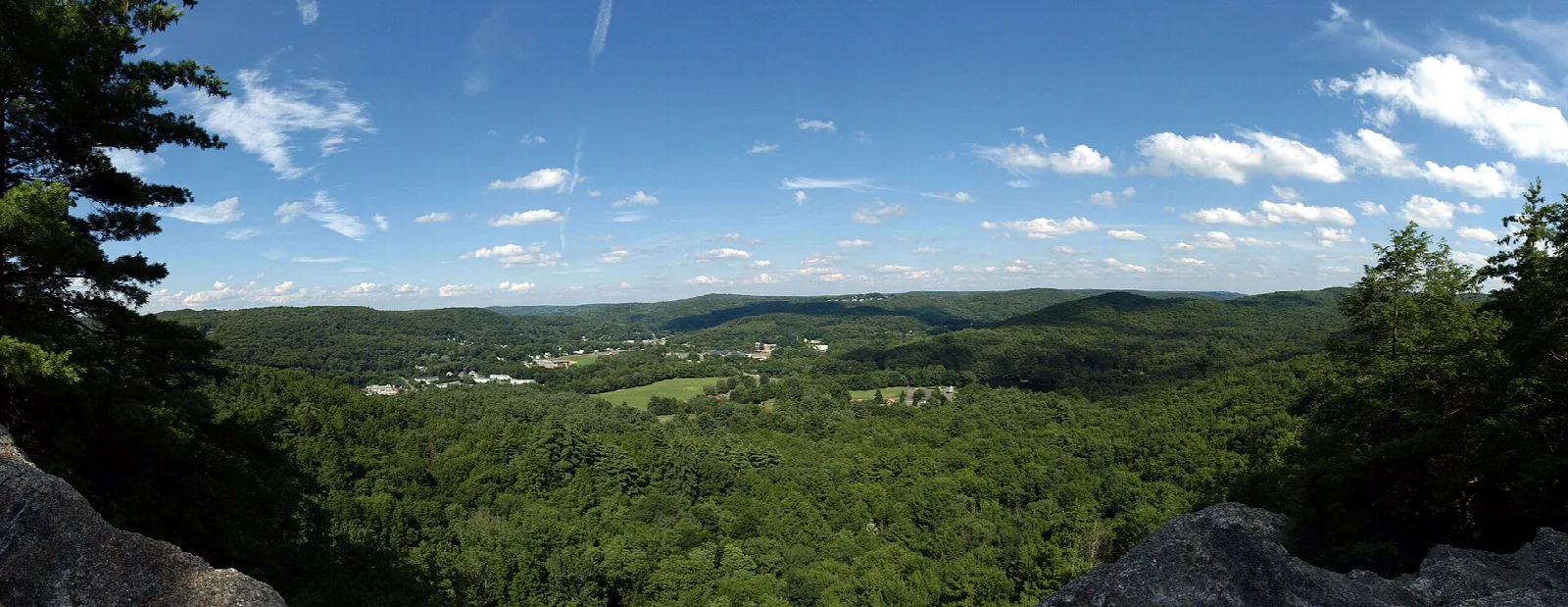 A wide green valley seen from a rocky lookout under blue sky