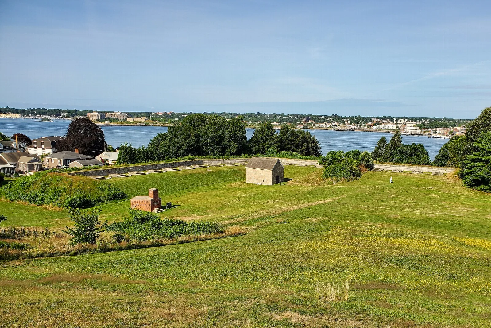 Grassy fort earthworks with a small stone building, with the river and city beyond