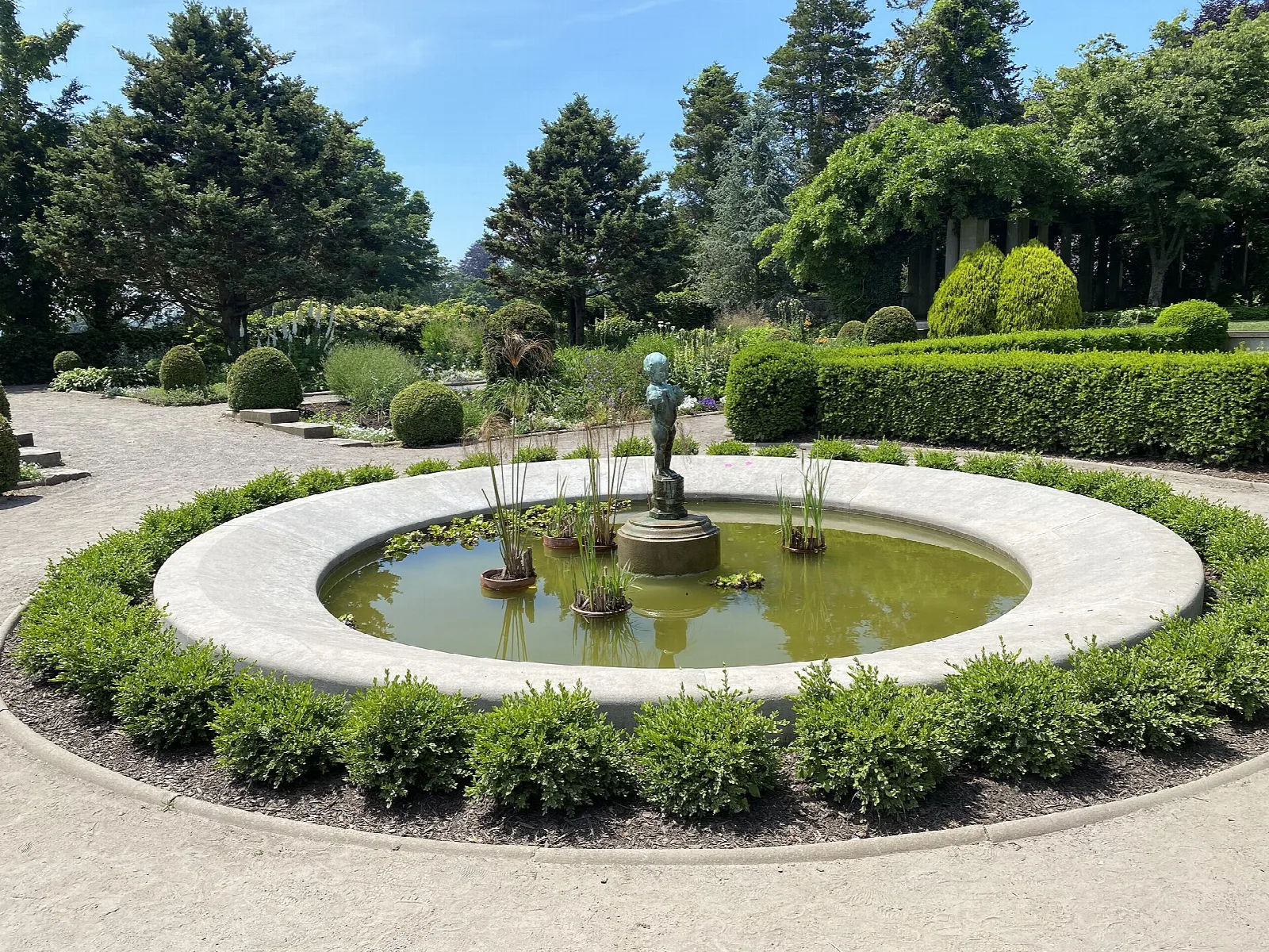 Round fountain pool inside a hedged formal garden