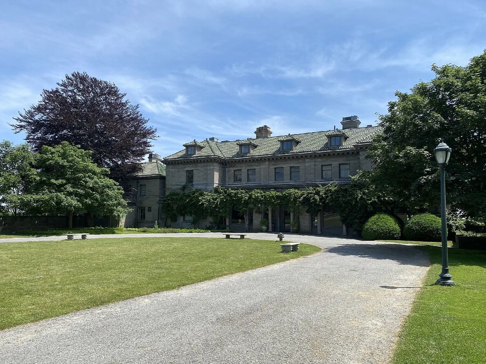 Long stone mansion beside a gravel drive and lawn