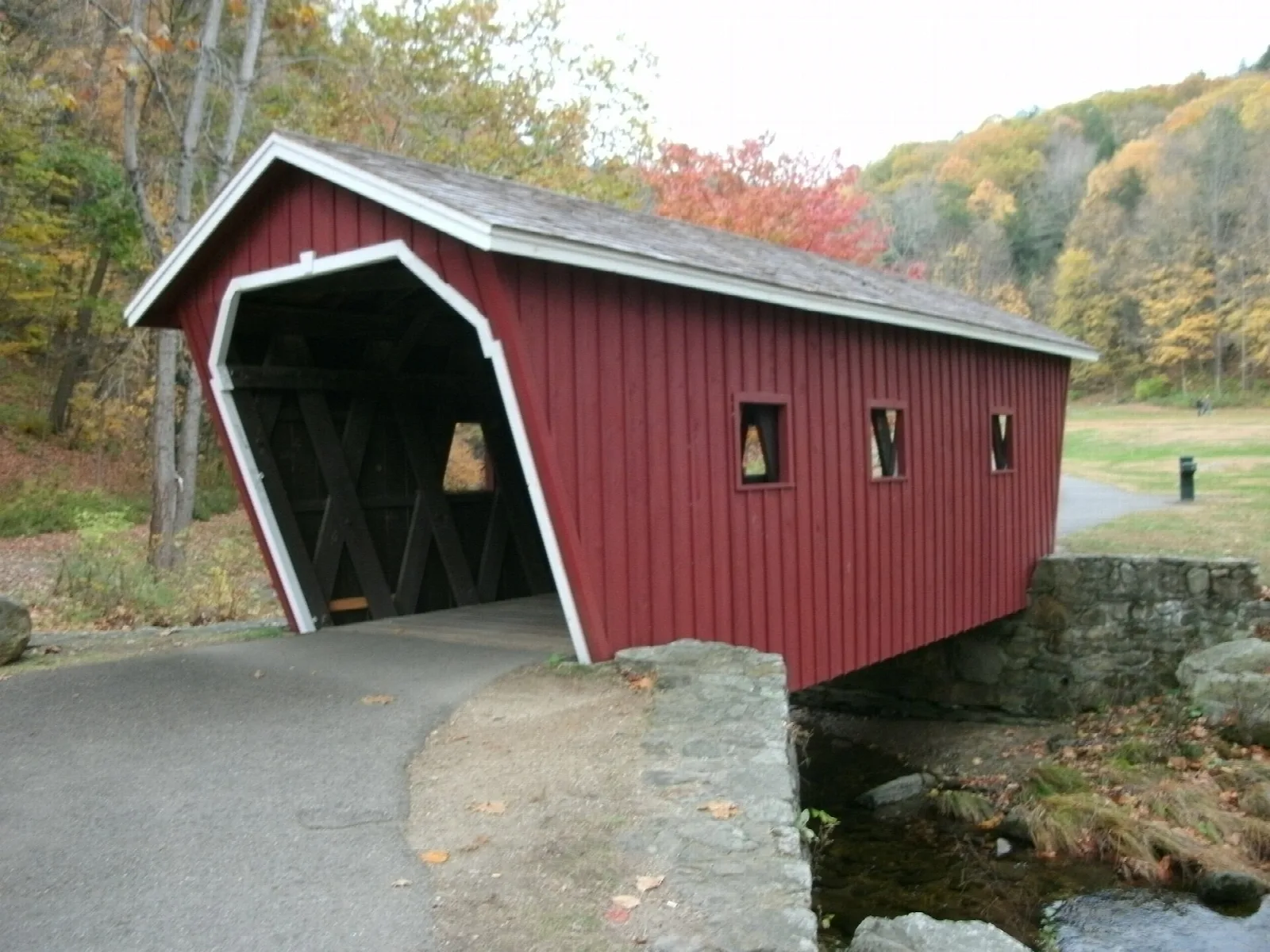 Red covered bridge by a paved path with fall foliage