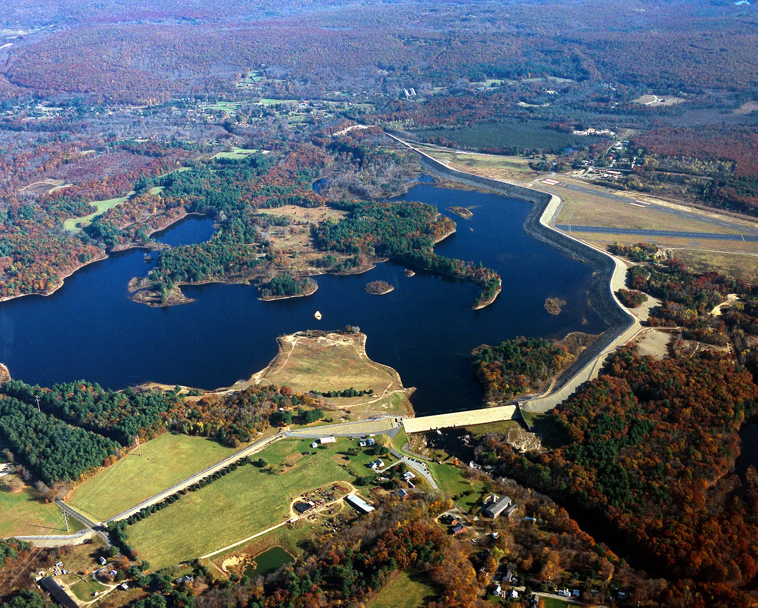 Aerial view of a lake with a dam and surrounding fields and forest