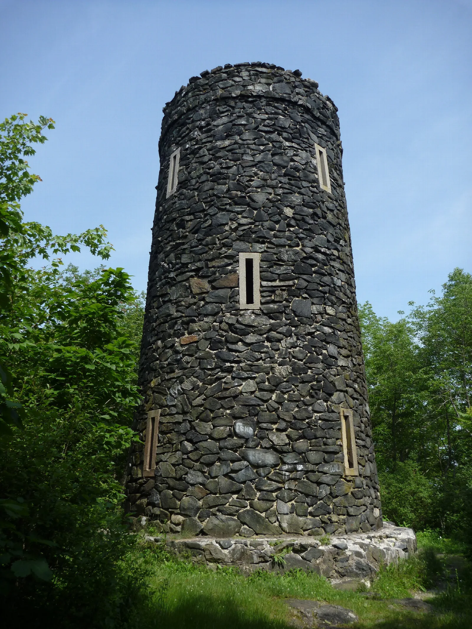 Round dark stone tower among green trees