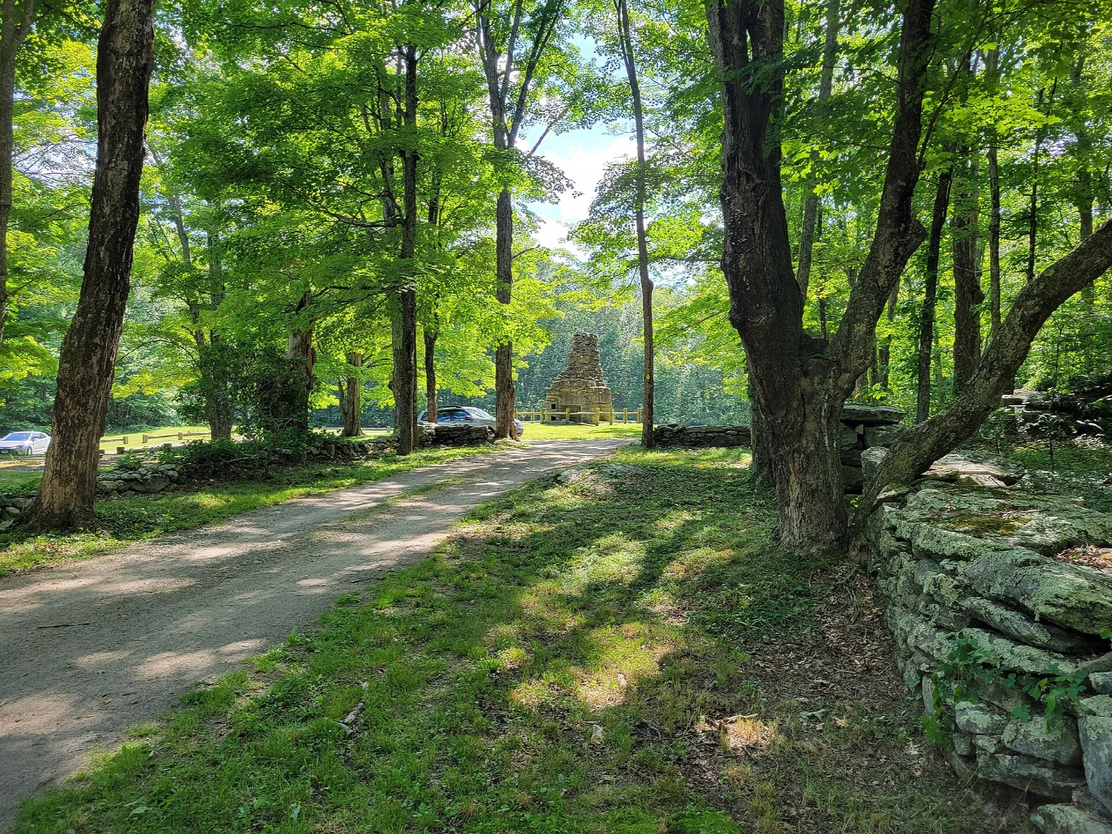 Dirt road past a stone wall with a chimney in the distance