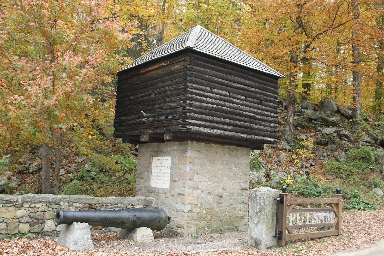 Log blockhouse on a stone base with a cannon beside it, autumn woods