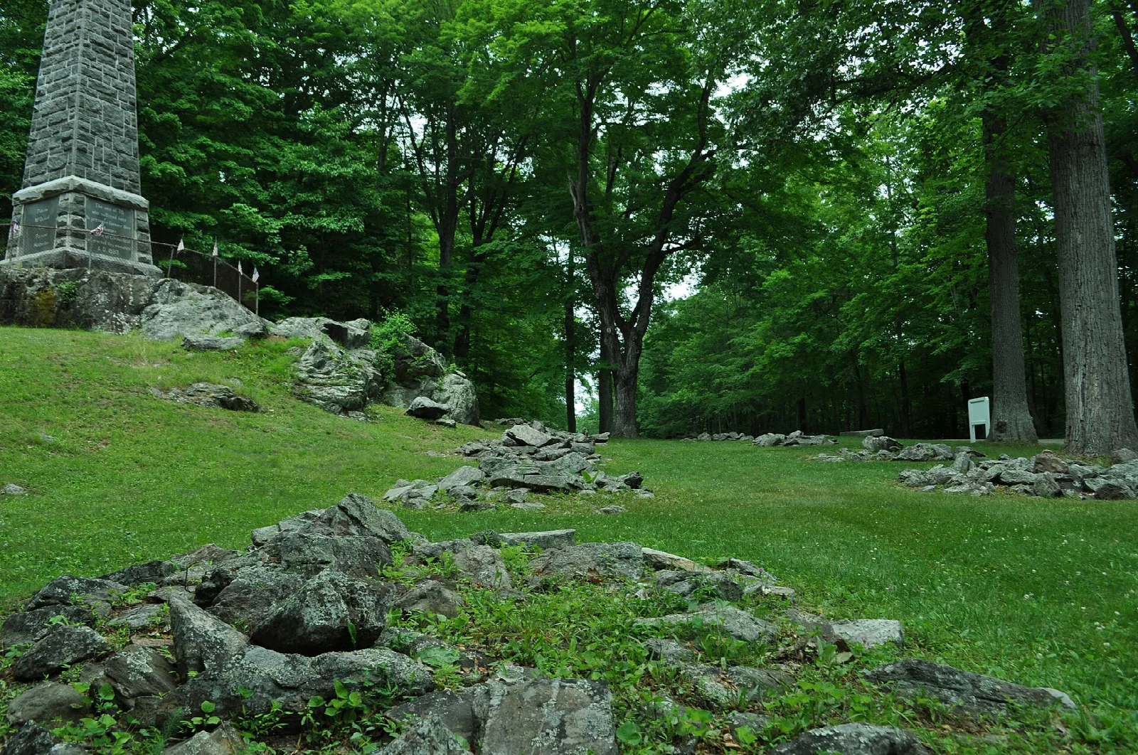 Grassy clearing with stone ruins and an obelisk among trees