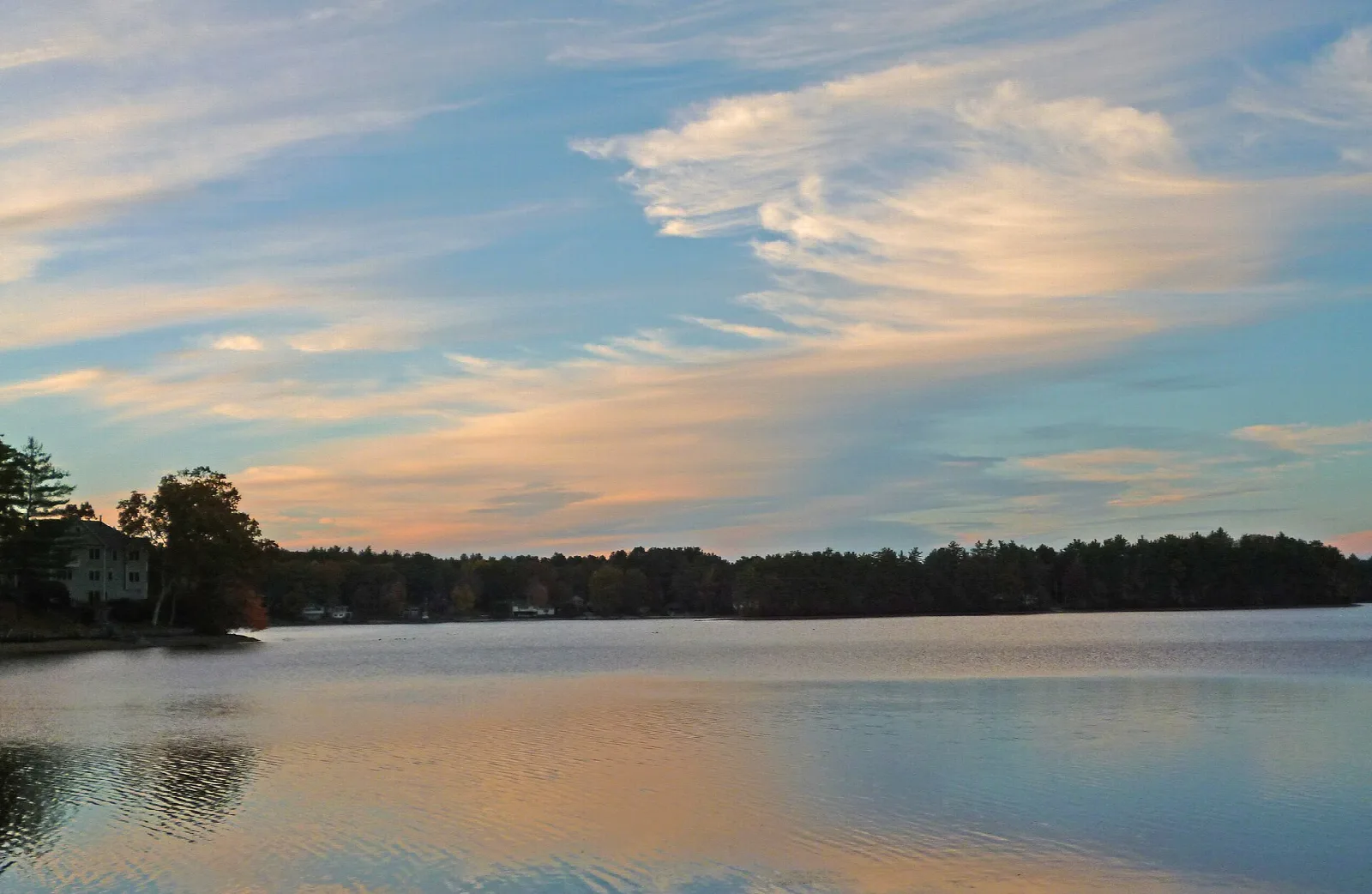 Wide reservoir at sunset with pink clouds and a wooded shore