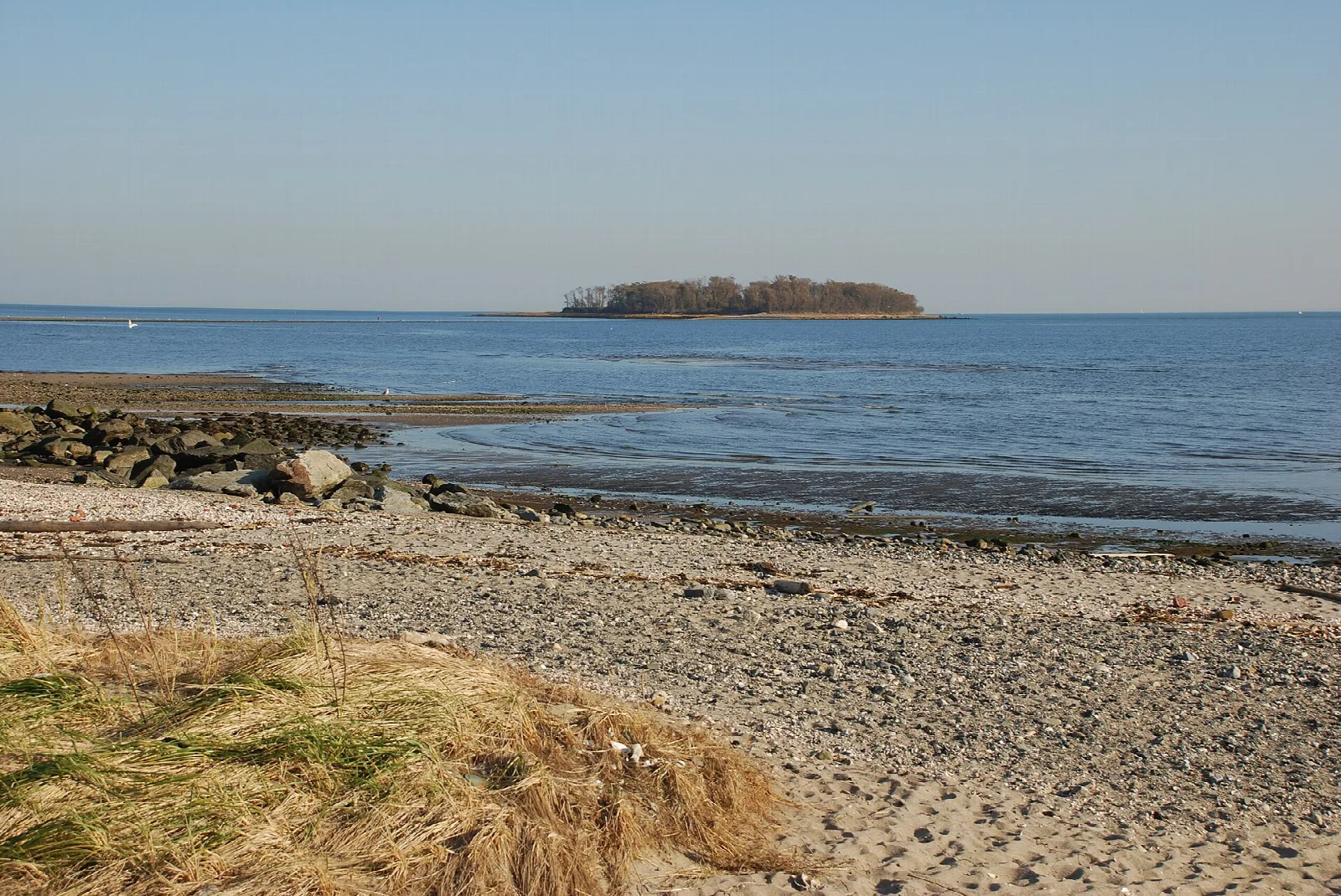 Small wooded island across gravel shore and calm water