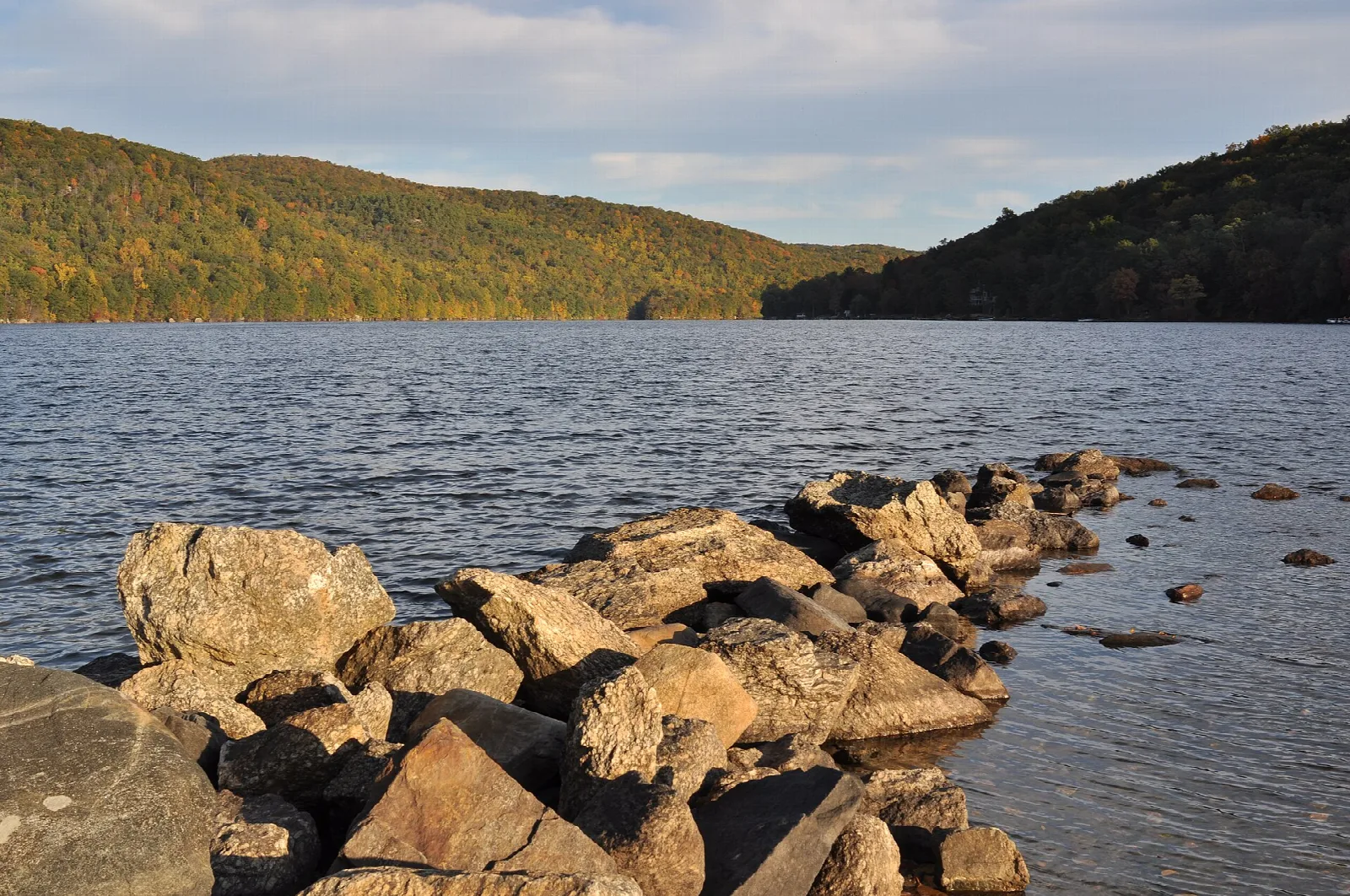 Lake with rocky shore and wooded hills under cloudy sky