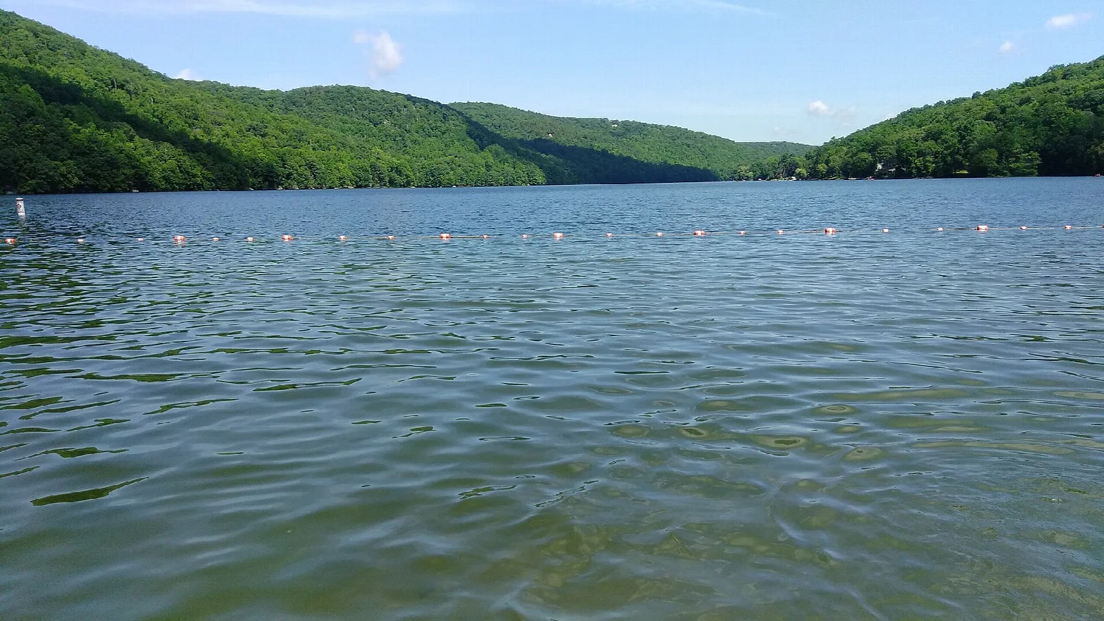 Wide lake with a swim line and green hills behind