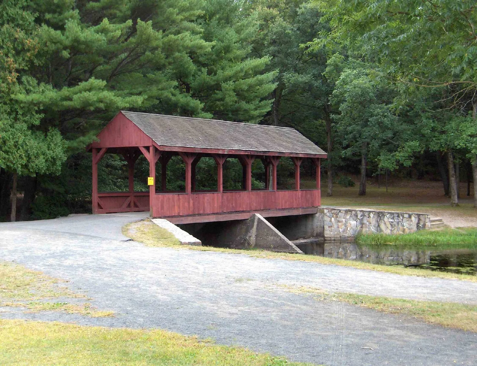 Red covered bridge walkway beside a gravel path among pines
