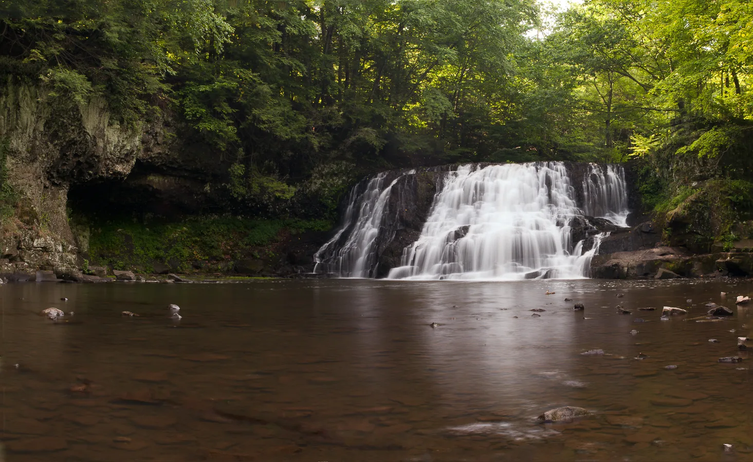 Wide waterfall spilling over a rock ledge into a pool