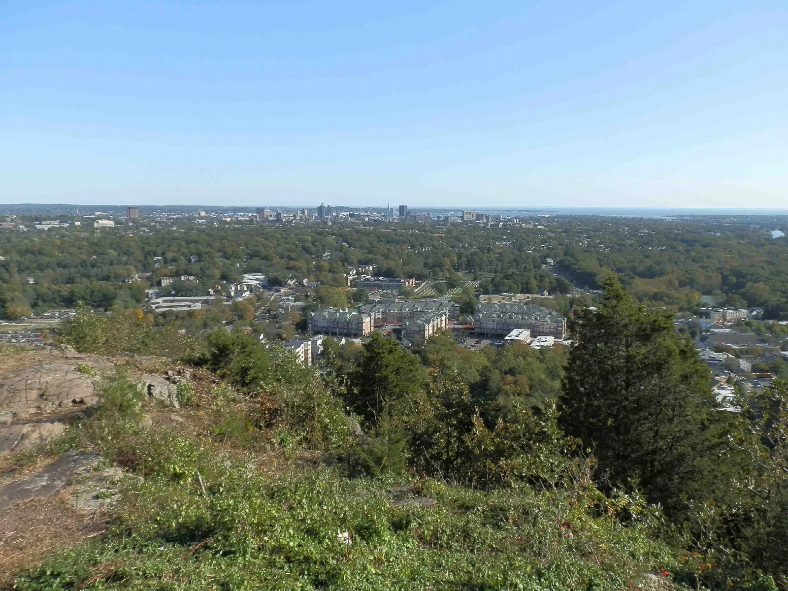 Town and trees seen from a rocky overlook under a blue sky