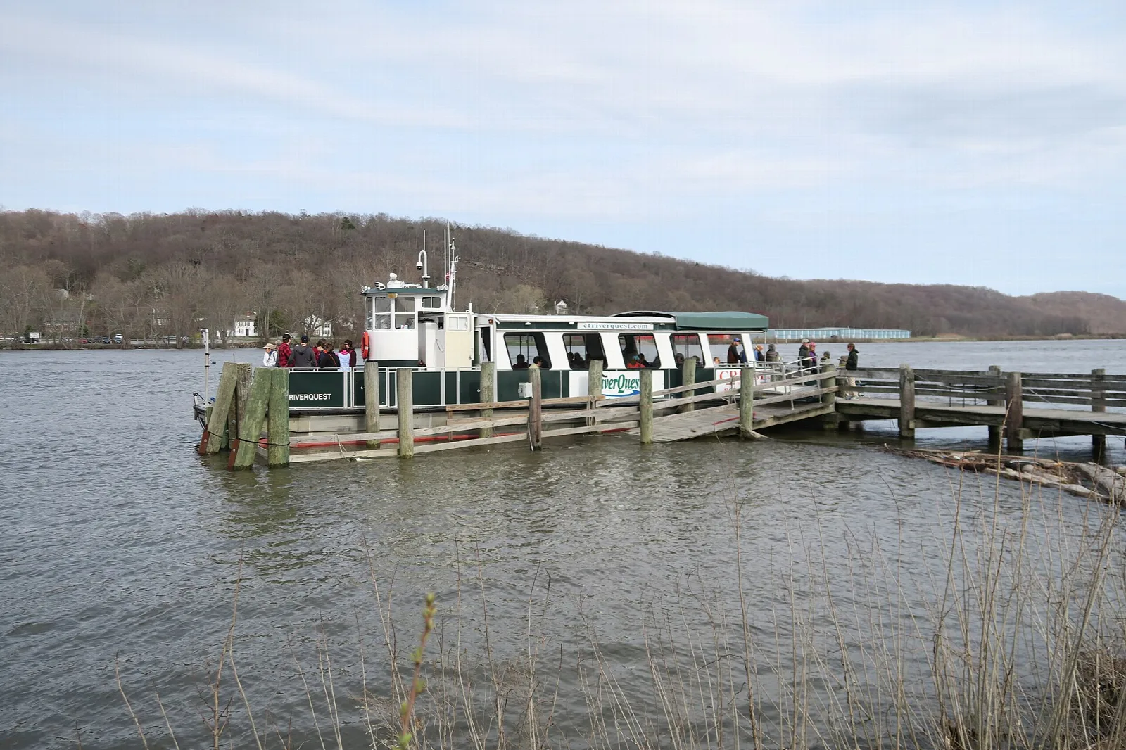Tour boat tied up at a wooden dock on the Connecticut River, with wooded hills beyond