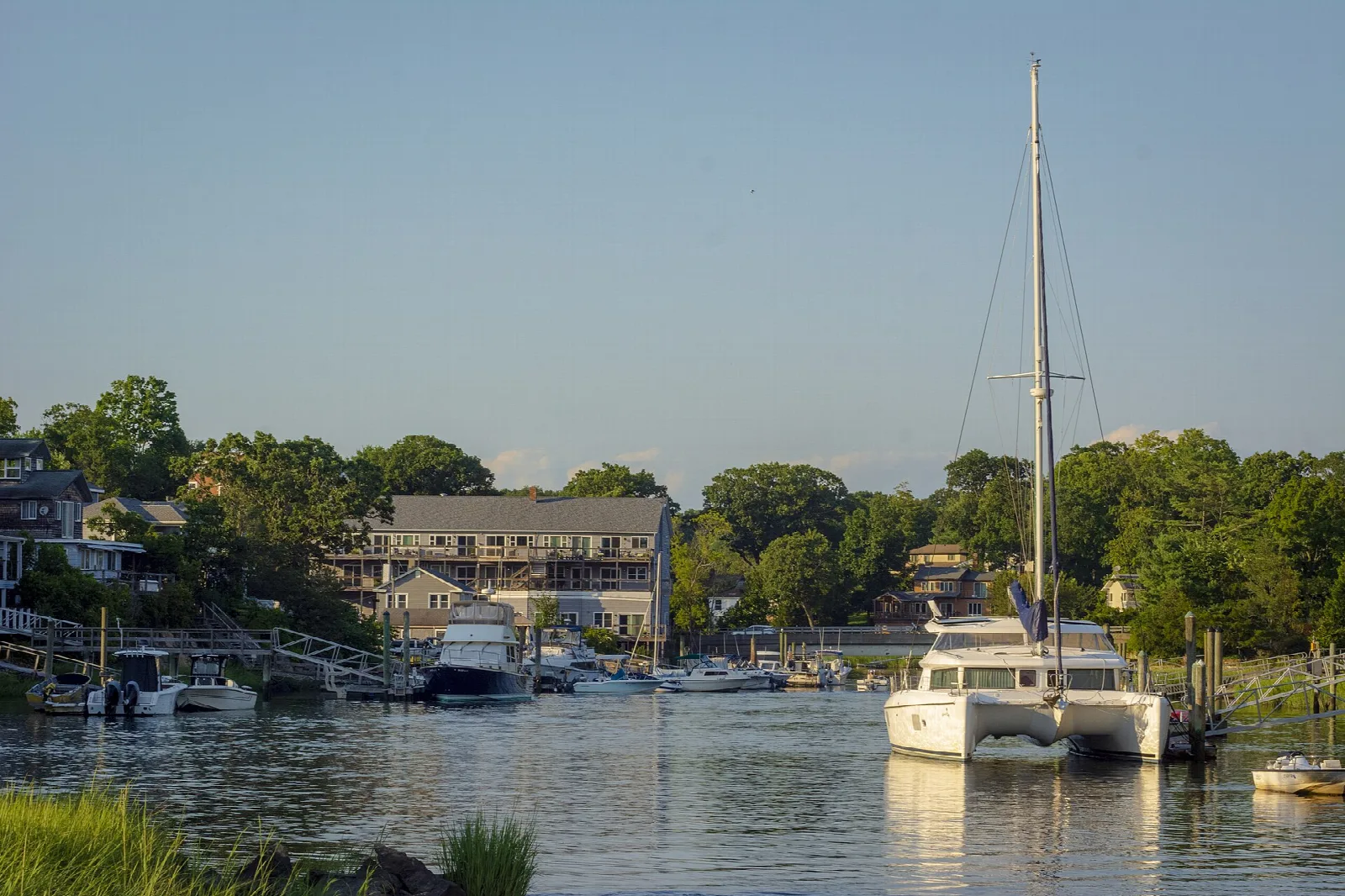 Sailboats and motorboats moored along the Farm River with houses and trees behind