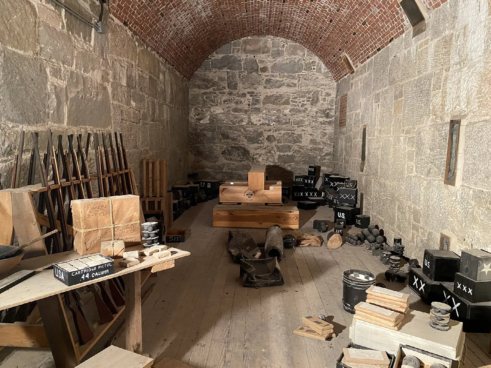 Vaulted brick and stone room holding wooden crates and equipment