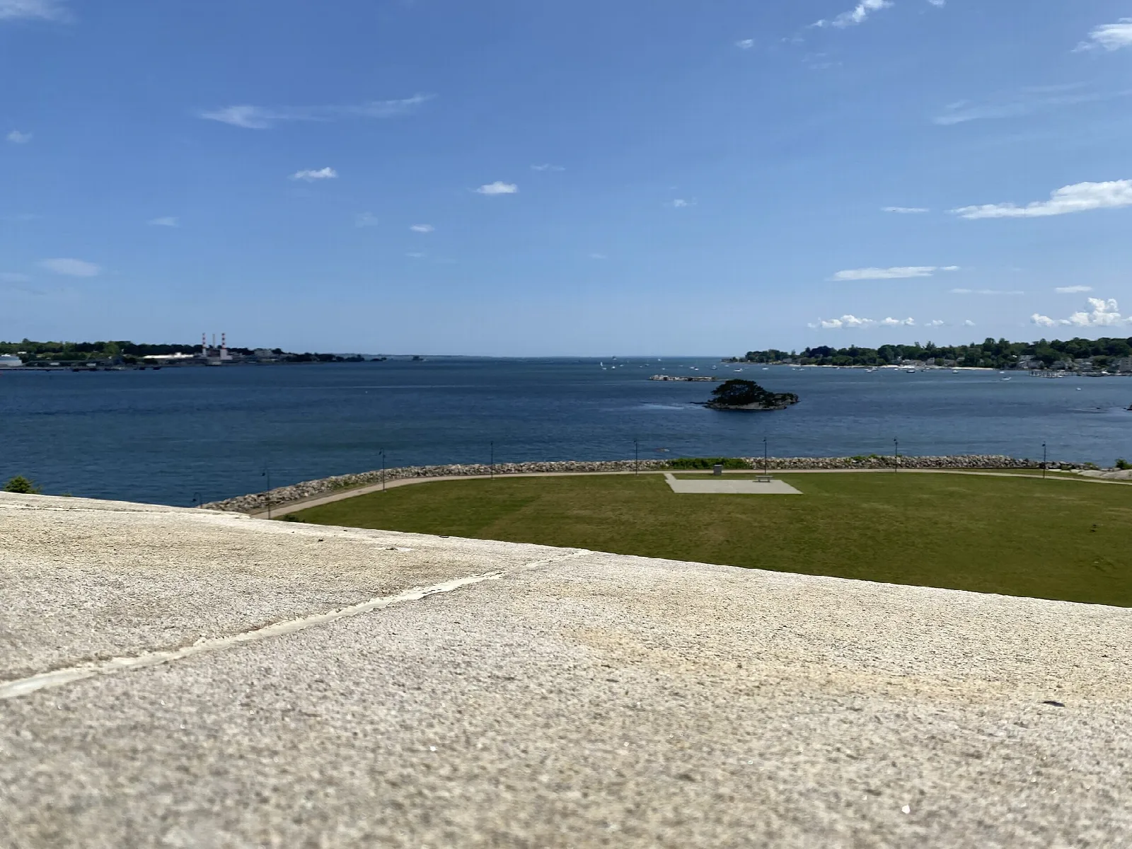 Grass and a stone walkway above a blue bay with a small island offshore