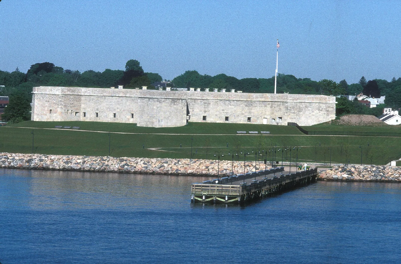 Long pale stone fort wall above a wooden pier and blue water