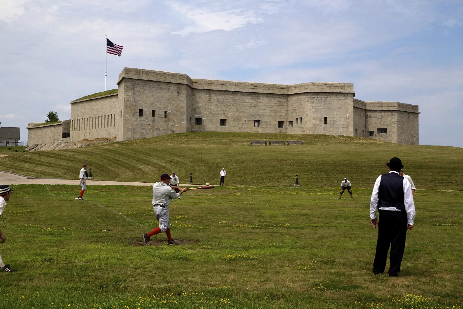 Granite fort behind a grassy field where people play baseball