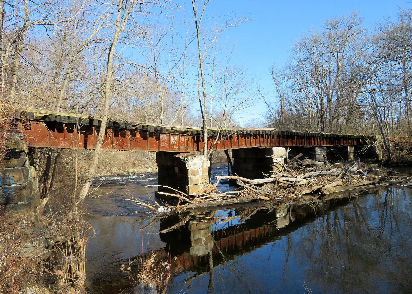 Rusted railroad bridge on stone piers over a river